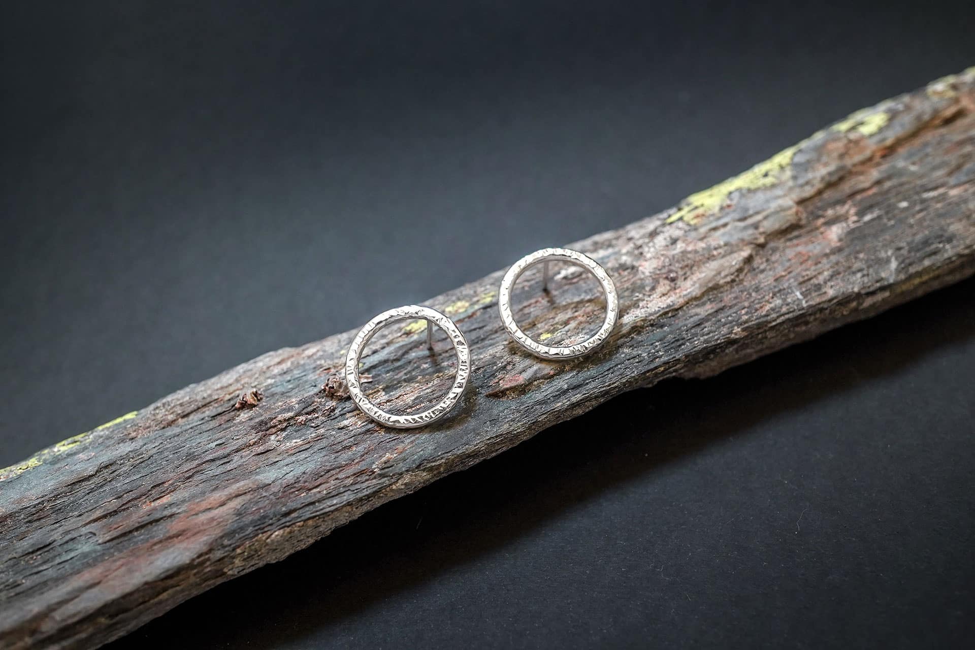 Pendientes de aro minimalistas con textura de plata de ley de Emeki Joyas, diseño contemporáneo colocado sobre la oreja, fotografiado sobre piedra con líquenes