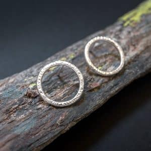 Detalle de la textura de pendientes de aro minimalistas en plata de ley de Emeki Joyas, diseño contemporáneo que se lleva colocado sobre la oreja, fotografiado sobre piedra con líquenes