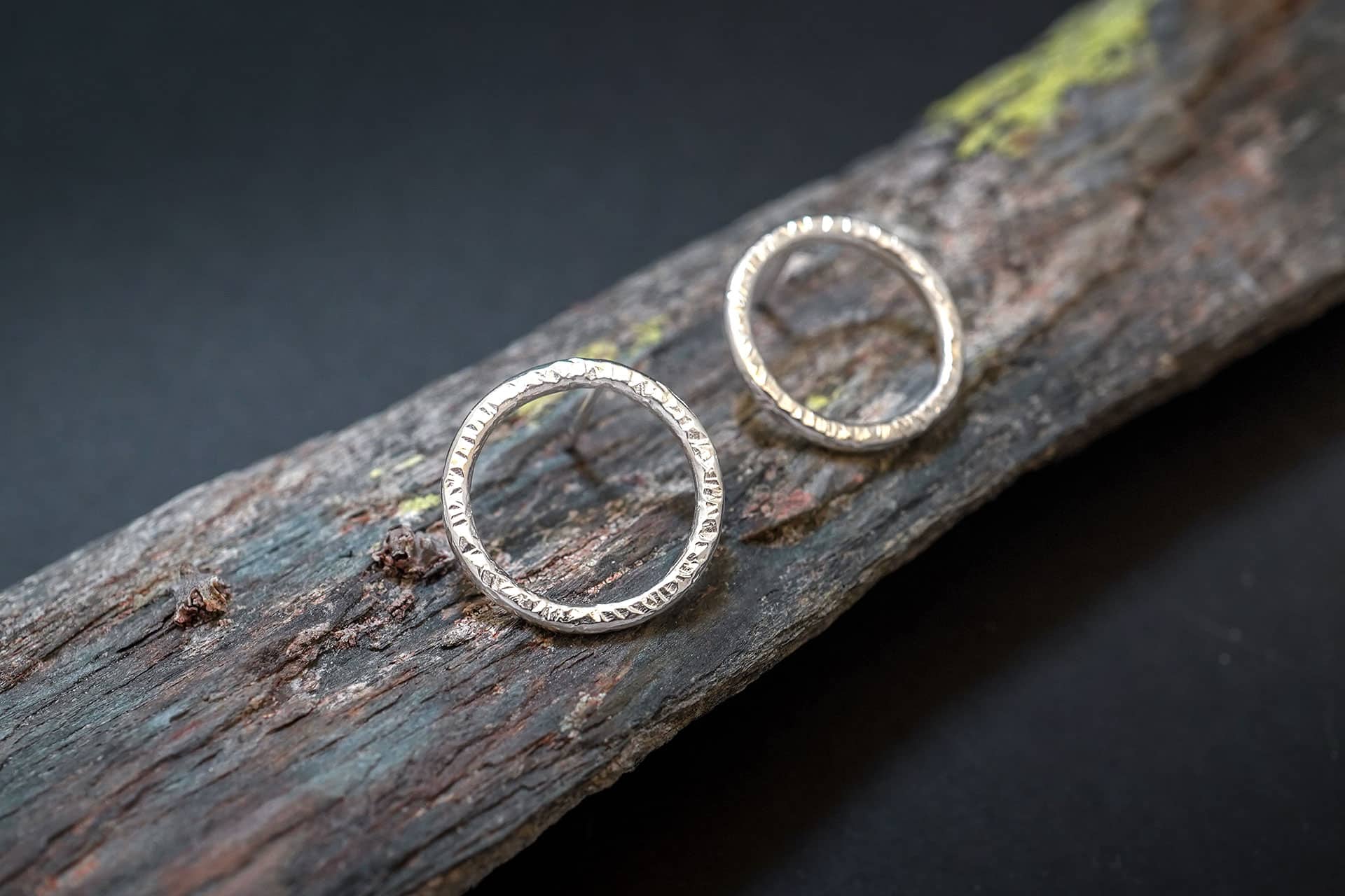Detalle de la textura de pendientes de aro minimalistas en plata de ley de Emeki Joyas, diseño contemporáneo que se lleva colocado sobre la oreja, fotografiado sobre piedra con líquenes