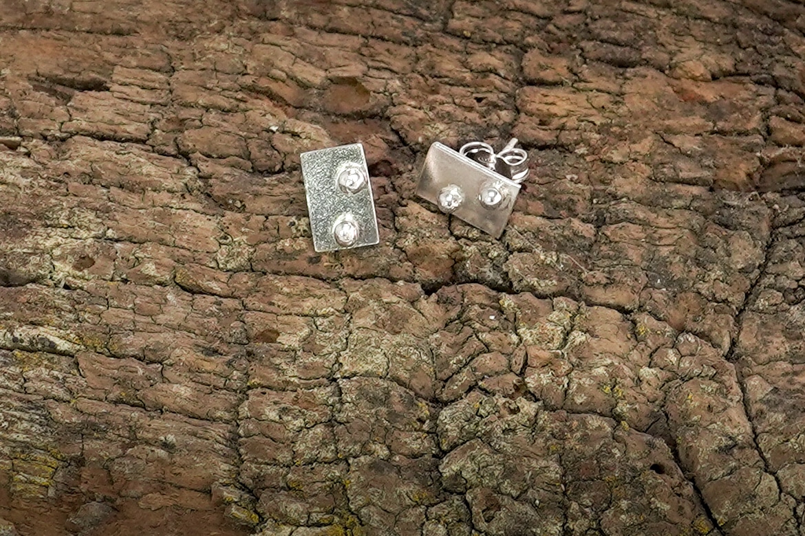 Pendientes Xirimiri Mini de Emeki Joyas, joyería artesanal en plata reciclada, diseño geométrico minimalista inspirado en gotas de lluvia fina ("xirimiri"), apoyados sobre madera.